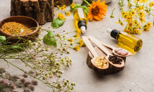 selective focus of wildflowers, herbs, bottles and pills in wooden spoons on concrete background,
